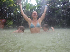 Veronique Rioux with her two boys in a pool while raining with her arms extended above her head and laughing