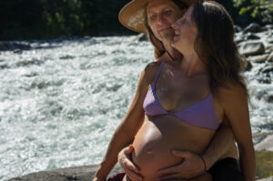 Veronique Rioux pregnant leaning back on her partner smiling at Nanaimo river