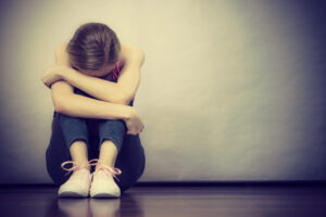 person sitting on the floor with her arms cross around her knee and head down hiding on her arms
