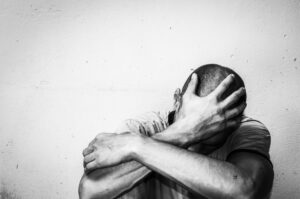a person sitting down with their head in one hand so we can't see their face and other arm wrapping around themselves